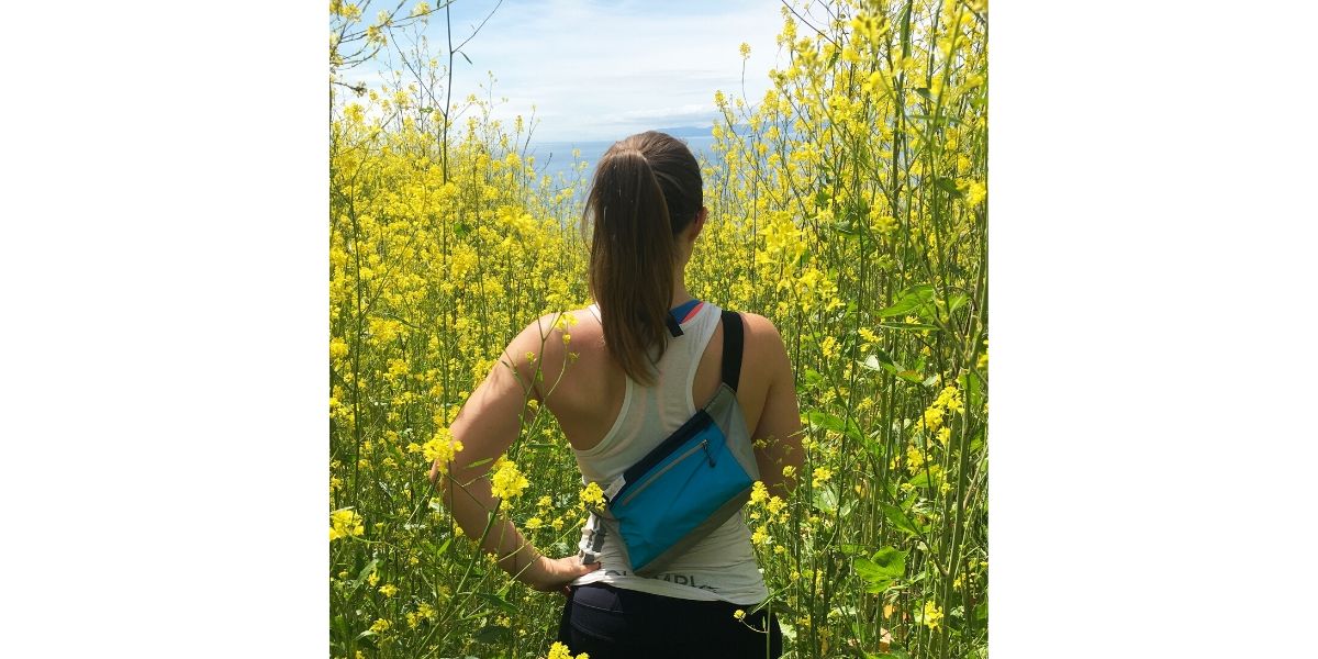 Woman wearing upcycled hip bag overlooking field of yellow flowers. 